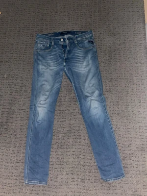 Ljusblå slim fit replay jeans - Säljer ett par ljusblå slim fit replay  jeans med klassisk femficksdesign och slitningar på benen. Jeansen har en snygg tvättad look och är tillverkade i denim. Perfekta för dig som gillar en avslappnad och trendig stil.