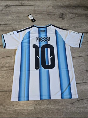 Argentina Messi matchtröja Adidas M - Säljer en  Argentina matchtröja från Adidas med Messi och nummer 10 på ryggen. Tröjan har klassiska blå och vita ränder, svarta detaljer och guldfärgade loggor på bröstet. Tillverkad i lätt och ventilerande material, perfekt för fotboll eller träning.