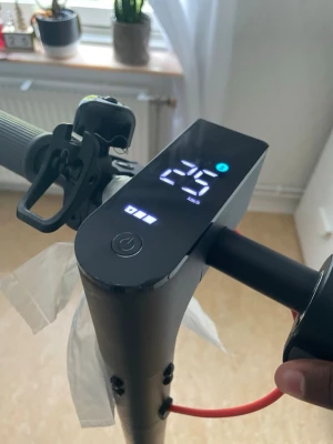Svart elscooter med digital display - Säljer en svart elscooter med tydlig digital display som visar hastighet och batterinivå. Scootern har gråa handtag, ringklocka och röd bromskabel. Perfekt för att ta sig runt i stan på ett smidigt sätt.
