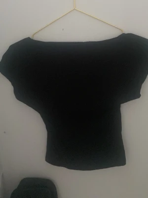 Svart offshoulder topp med öppen rygg - Snygg svart offshoulder topp med bred halsringning och figurnära passform. Perfekt att styla med höga jeans eller kjol för en trendig look. Tunn och mjuk i materialet, enkel att matcha till olika outfits.