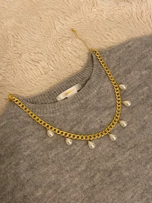 Guldhalsband med droppformade pärlor - Snyggt halsband i guldfärgad rostfritt med droppformade pärlor som hänger längs kedjan. Perfekt för att ge din outfit en trendig och elegant touch. Kedjan är chunky och pärlorna ger en lyxig känsla.