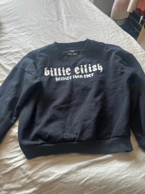 Svart Billie Eilish sweatshirt - Cool svart sweatshirt med tryck fram och bak från Billie Eilish 'Happier Than Ever'. Oversized fit med ribbade muddar vid ärmslut och nederkant. Perfekt för dig som gillar streetwear och vill ha något unikt i garderoben.