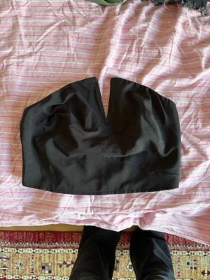 Svart axelbandslös tubtopp med v-ringning - Snygg svart axelbandslös tubtopp med markerad v-ringning framtill och dragkedja bak. Toppen har en croppad passform och är perfekt att styla till höga jeans eller kjol. Gjord i ett slätt och stretchigt material för en bekväm känsla.