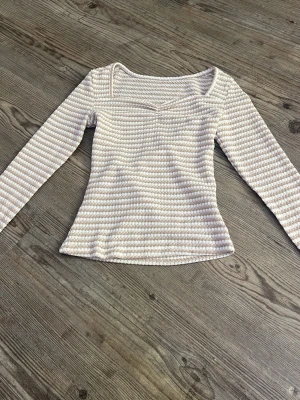 Ljusrandig långärmad topp - Säljer en långärmad topp med ljusa ränder och v-ringad hals. Toppen har en figurnära passform och är tillverkad i ett mjukt, stretchigt material. Perfekt för dig som gillar stilrena och bekväma plagg.