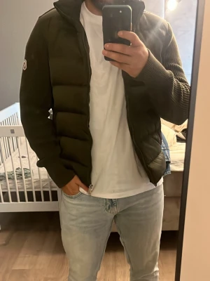Olivgrön Moncler cardiganjacka - Snygg olivgrön cardiganjacka från Moncler med vadderad front och stickade ärmar. Dragkedja framtill och Moncler-logga på vänster ärm. Perfekt för lager-på-lager och ger en sportig men stilren look. NFC BLIPP allt funkar, använd några gånger och inga skador eller så 