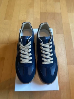 Marinblå sneakers Gats - Snygga marinblå sneakers med beige snörning och gummisula. Ovandelen är i en mix av mocka och slätt läder för en stilren outfit och original box medföljer utan en annan. Perfekta för dig som vill ha klassiska men ändå trendiga skor till vardagsoutfiten.