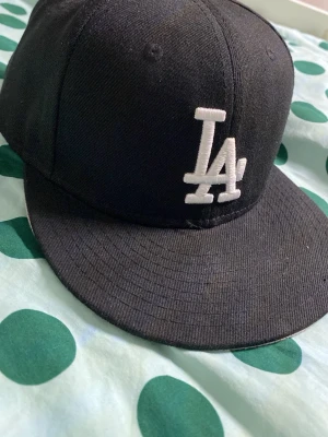 Svart LA keps Cooperstown Collection - Snygg svart keps med vit LA-logga framtill. Klassisk rak skärm och broderad ventilation på ovansidan. Märkt med Cooperstown Collection på insidan. Perfekt för dig som gillar sportig och stilren streetwear.