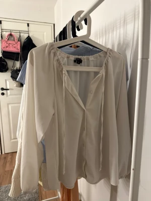 Vit blus  - Säljer en elegant vit blus från Wearewomen i storlek S. Blusen har långa ärmar, knappar framtill och en fin rynkad detalj vid halsen med knytband. Skriv vid frågor.