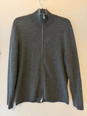 Grå ziptröja från H&M - Snygg grå ziptröja från H&M med hög krage och hel dragkedja. Tröjan är i mjukt stickat material och har en enkel, stilren design som passar perfekt till lager-på-lager. Perfekt för kyliga dagar och enkel att matcha med andra plagg.