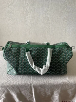 Grön weekendbag - Snygg grön weekendbag med vitt grafiskt mönster och vita handtag. Väskan har dragkedja upptill och är rymlig nog för resor eller gymmet. Tillverkad i slitstarkt material och har en modern, stilren look.