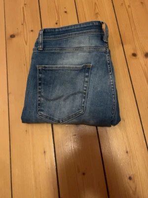 Blå jeans från Jack & Jones - Säljer ett par blå jeans från Jack & Jones med klassisk femficksmodell och snygg slitning framtill. Jeansen har normal midja, raka ben och är tillverkade i denim med en lätt tvättad look. Perfekta för en avslappnad stil. ‼️Den har lite fläckar på bak fickorna men det är inget man lägger märke til‼️