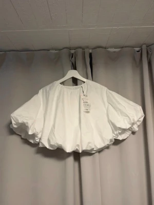 Vit croppad blus med volangärm - Säljer en vit croppad blus med stora volangärmar och rund hals. Toppen har en luftig och oversized passform som ger en cool och trendig look. Perfekt att styla med höga jeans eller kjol.