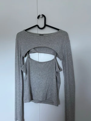 Grå långärmad topp med cut out-detalj - Toppen och linnet sitter inte ihop. Så man kan använda de var för sig också. Trendig grå långärmad topp med unik cut out-detalj över bröstet och inbyggd ärmlös topp under. 
