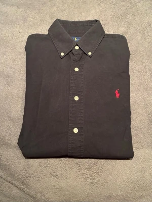 Ralph Lauren skjorta - Skjorta från Ralph Lauren | Storlek: M | Färg: Svart med röd logga | Fint skick, lite svett märken vid armhålan | Skriv vid frågor | Paketpris vid köp av flera varor |