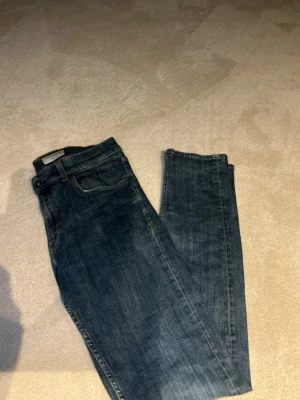 Mörkblå raka jeans - Säljer ett par mörkblå jeans med rak passform och klassisk femficksdesign. Jeansen har en snygg tvättad look och är tillverkade i denim. Perfekta till vardags för en avslappnad stil.