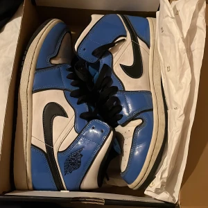 Nike Air Jordans i blått och vitt - Säljer ett par snygga Nike Air Jordans i blått och vitt. Skorna har en klassisk design med svart snörning och den ikoniska Nike-loggan på sidan. Perfekta för både vardag och fest!