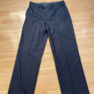 Svarta kostymbyxor från Lapidus - Säljer ett par stiliga svarta kostymbyxor från Lapidus. De har en klassisk design med raka ben och en knappstängning i midjan. Perfekta för både formella tillfällen och kontoret. Byxorna har en elegant passform och är gjorda i ett bekvämt material.