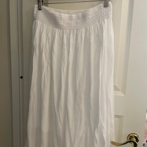 Vit långkjol från Opposite Blue - Säljer en superfin vit långkjol från Gypsie Blue. Kjolen har en elastisk midja med ett snyggt smockmönster som ger en bekväm passform.  Storlek L, men mer som M-S. Perfekt för sommaren eller utomlands. Den har ett litet hål längst ned, men lättlagat.