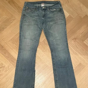 Vintage True Religion #32 - Vintage True Religion jeans som är väldigt snyggt slitna i precis rätt färg och som de bör vara. Bootcut och midwaist. Hål på höger lår. Fattas knapp på vänster bakficka. Midja ca. 43/86cm Inre benlängd ca. 80cm Yttre benlängd ca. 104 Nedtill ca 24cm