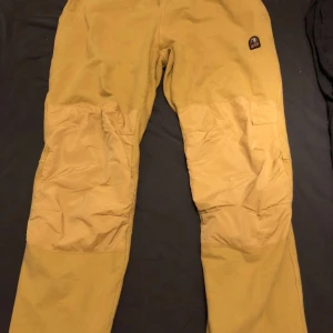 Gula fleecebyxor från Parajumpers - Säljer ett par sköna och varma gula fleecebyxor från Parajumpers. Byxorna har en elastisk midja och en liten ficka bak. Perfekta för kalla dagar eller mysiga hemmakvällar. Märket PJS är broderat på sidan. Passa på att köpa dessa unika byxor!