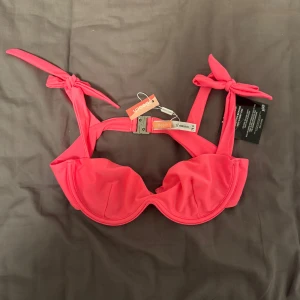 Röd bikiniöverdel från Nelly - Säljer en snygg neon rosa bikiniöverdel från Nelly i storlek 75C. Den har knytband vid axlarna och en praktisk spänne i ryggen. Perfekt för sommarens alla badäventyr! 💦