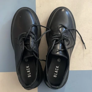 Svarta snörskor i skinn - Säljer ett par stilrena svarta snörskor. Veganska. De har en robust sula och klassisk design som passar perfekt för både vardag och fest. Skorna är i nyskick och har en snygg, blank yta. Perfekta för dig som vill ha en tidlös look!