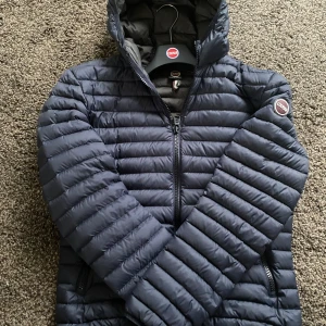 Mörkblå jacka från Colmar - Säljer en snygg mörkblå jacka från Colmar. Jackan har en quiltad design med dragkedja och huva. Storlek 48 vilket motsvarar storlek (S) 