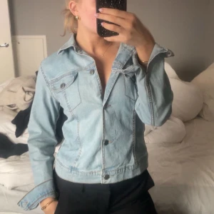 Ljusblå jeansjacka - Säljer en snygg ljusblå jeansjacka med klassisk krage och knappar framtill. Jackan har långa ärmar och två bröstfickor med knappstängning. Perfekt för en avslappnad stil. Funkar även som jeansskjorta som jag har på bilden. Den är aldrig använd.
