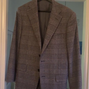 Rutig kavaj från Corneliani - Snygg rutig kavaj från Corneliani i grått och svart. Perfekt för en stilren look med klassiska rutor och två knappar framtill. Tillverkad i Italien, vilket garanterar hög kvalitet och stil. Passar utmärkt för både formella och semi-formella tillfällen. 100% ull.