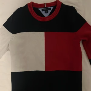 Flerfärgad tröja från Tommy Hilfiger - Säljer en snygg flerfärgad tröja från Tommy Hilfiger. Tröjan har blockmönster i svart, rött och vitt med en ribbad krage. Perfekt för en stilren look.