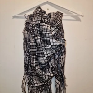 Svartvit rutig halsduk - Snygg och stilren svartvit rutig halsduk med fransar. Perfekt för att hålla sig varm och trendig under kyliga dagar. Den har ett klassiskt rutmönster som passar till många olika outfits.