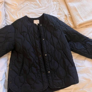 Svart quiltad jacka från H&M - Säljer en svart quiltad jacka från H&M i storlek M. Jackan har en stilren design med knappar framtill och långa ärmar. Perfekt för kyligare dagar och ger en snygg look. 🖤
