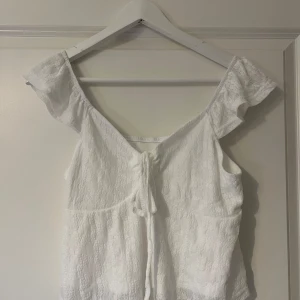 Vit blus med knyt - Vit blus/topp med knytning i fram, storlek L passar S/M. Aldrig använd. 15kr + frakt