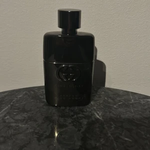 Gucci Guilty Pour Homme Eau de Parfum - Elegant och maskulin parfym från Gucci i en stilren svart flaska. Doften är intensiv och sofistikerad, perfekt för den moderna mannen. Flaskan har en glansig finish med Guccis ikoniska logotyp ingraverad på framsidan. Ungefär 70 procent av parfymen återstår.