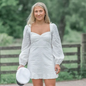 Vit klänning med puffärmar - Säljer min studentklänning från Nelly. En söt vit klänning med puffiga långärmar och volangdetaljer. Klänningen har en v-ringad design och knytning i ryggen. Perfekt för studenten och sommaren.