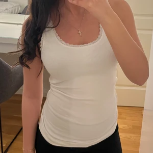 Vit linnetopp med spetsdetaljer - Säljer en stilren vit linnetopp med fina spetsdetaljer längs halsringningen och ärmhålen. Perfekt för en enkel och fräsch look. Passar bra till både jeans och kjol.