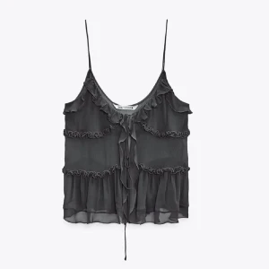 Svart volangtopp från Zara - Säljer en svart topp från Zara med tunna axelband och volangdetaljer. Toppen har en luftig design med knytning framtill och är perfekt för varma dagar. Den är omsydd för en bättre passform så skriv för mer bilder på de!