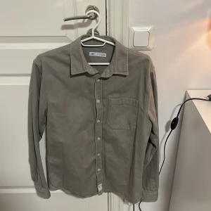  Zara - Snygg grå skjorta från Zara i en klassisk design med krage och knappar framtill. Skjortan har en bröstficka och långa ärmar, perfekt för en stilren look. Tillverkad i ett mjukt material som ger en bekväm passform.