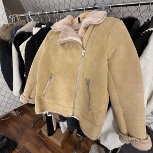 Beige mockajacka med foder - Snygg beige mockajacka med mjukt foder och dragkedja. Jackan har en klassisk look med två fickor framtill och en skön krage. Perfekt för kyligare dagar.