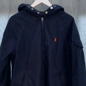 Ralph Lauren Vår Jacka - Säljer denna snygga Ralph lauren jackan i marinblå 💯Storlek M | Skick 8/10 jackan saknar en knapp på arm fickan (se sista bild) och snörena men annars inga fler defekter | Tveka inte fråga vid funderingar 💭 (Pris kan diskuteras)