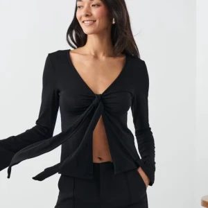 Svart långärmad topp med knyt - Snygg svart långärmad topp med knyt framtill och v-ringning. Perfekt för en stilren look.