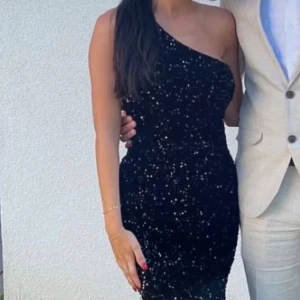 Svart glittrig långklänning - Säljer en elegant svart långklänning med glittrigt mönster. Klänningen är oneshoulder och har en figurnära passform som ger en snygg siluett. Perfekt för en festlig kväll! ✨