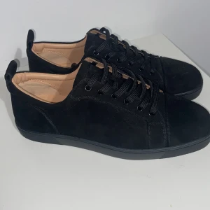 Svarta sneakers från Christian Louboutin - Snygga svarta sneakers i mocka från Christian Louboutin med den ikoniska röda sulan. Skorna har snörning och en stilren design som passar perfekt för en trendig look.