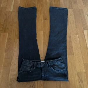 Svarta jeans från Gina Tricot - Snygga low waist och bootcut svarta jeans från Gina Tricot i en klassisk design. De har en normal passform med dragkedja och knapp framtill. Perfekta för en stilren look.