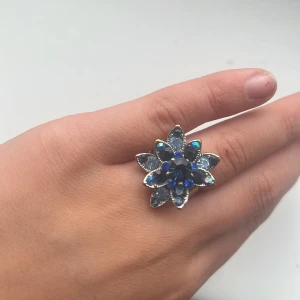 Blå blomformad ring - Snygg ring i form av en blomma med blå och silverfärgade stenar. Använder inte silver längre,har använt den kanske 7 gånger tidigare 