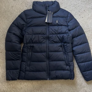 Mörkblå dunjacka från Polo Club  - Säljer en snygg mörkblå dunjacka från Polo Club med dragkedja och medelhög krage. Jackan har två praktiska fickor med dragkedjor och en liten broderad logga på bröstet. Helt oanvänd! Köpt på Zalando för 1103kr, mitt pris 890kr. Perfekt för kyliga dagar! 💙