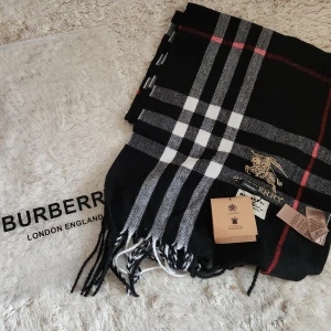 Svart rutig halsduk från Burberry - Elegant svart halsduk från Burberry i 100% kashmir. Den har ett klassiskt rutigt mönster i vitt och rött med fransar i ändarna. Perfekt för att hålla dig varm och stilren under kyliga dagar.