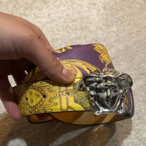 Färgglatt bälte med silverdetalj - Snyggt bälte med ett färgglatt mönster i lila, gult och rött. Bältet har en iögonfallande silverspänne med ett unikt designmotiv. Perfekt för att ge din outfit en färgklick och stil.