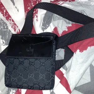 Svart axelväska från Gucci - Snygg svart axelväska från Gucci med det klassiska GG-mönstret. Väskan har en justerbar axelrem och en praktisk dragkedja för säker förvaring. Perfekt för att bära dina nödvändigheter med stil.