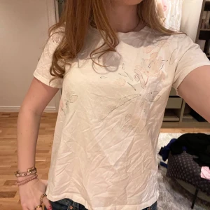 Vit t-shirt med blommigt mönster - Säljer en vit t-shirt med ett blommigt mönster. Den är lite skrynklig men stryker såklart innan jag skickar. 